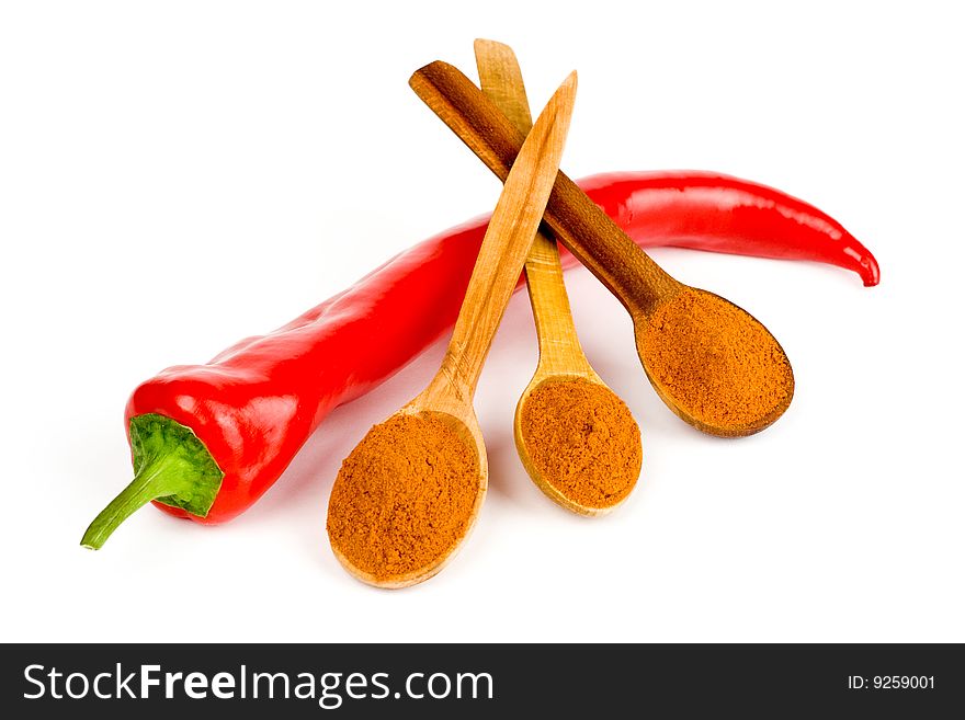 A composition of a pod of red chile pepper and three wooden spoonful of red ground pepper on a white background. A composition of a pod of red chile pepper and three wooden spoonful of red ground pepper on a white background