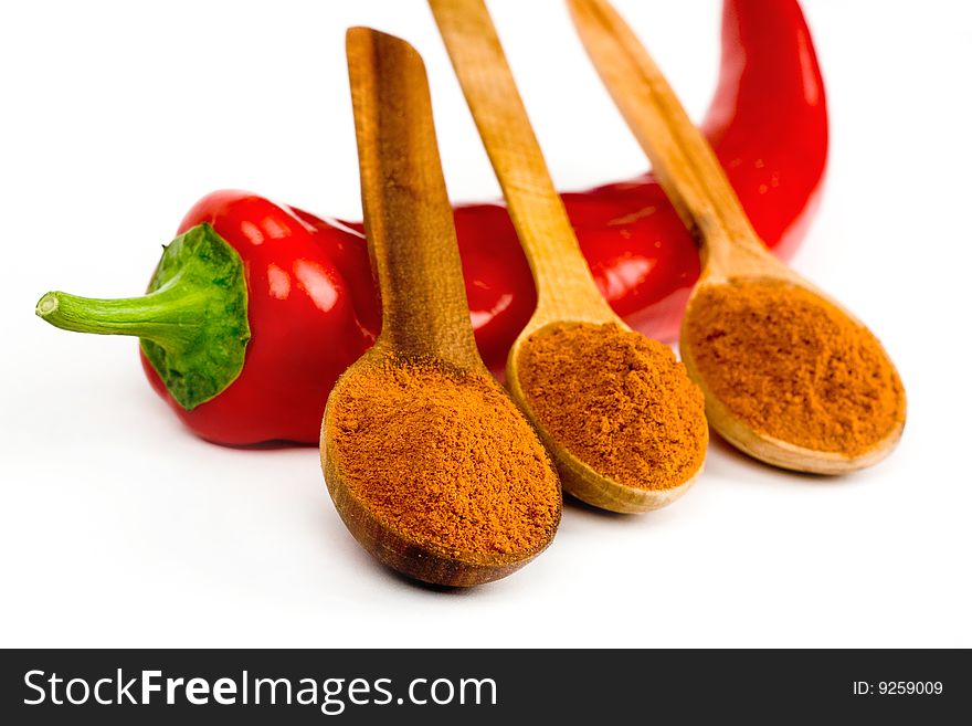 A pod of red hot chili and three wooden spoonful of ground red pepper across it on a white background. A pod of red hot chili and three wooden spoonful of ground red pepper across it on a white background