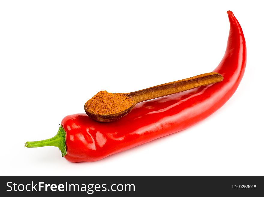 A composition of a wooden spoonful of ground red  pepper on a pod of red chile pepper on a white background. A composition of a wooden spoonful of ground red  pepper on a pod of red chile pepper on a white background