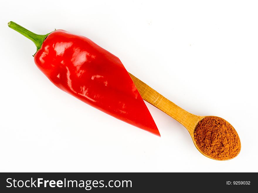 A composition of a pod of red  chili  on a wooden spoonful of ground red  pepper on a white background. A composition of a pod of red  chili  on a wooden spoonful of ground red  pepper on a white background