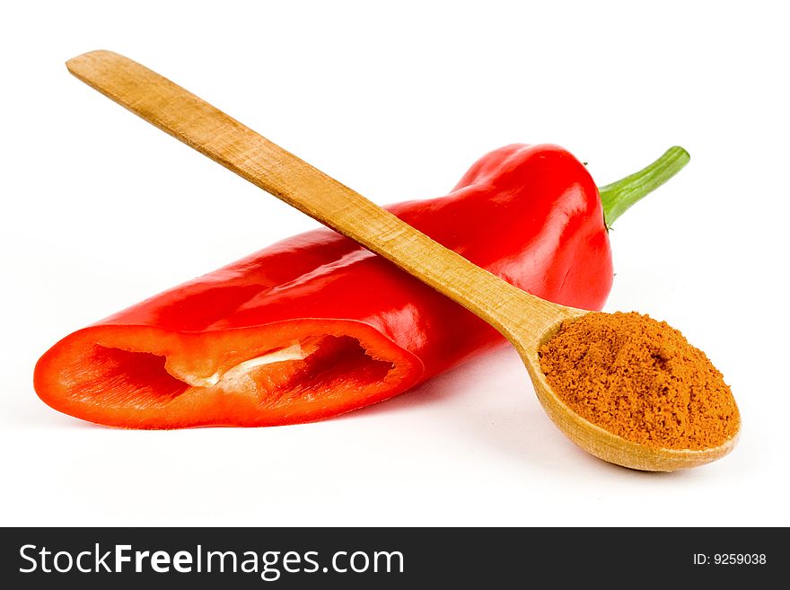 A composition of a wooden spoonful of ground red  pepper across a pod of red Chile pepper on a white background. A composition of a wooden spoonful of ground red  pepper across a pod of red Chile pepper on a white background