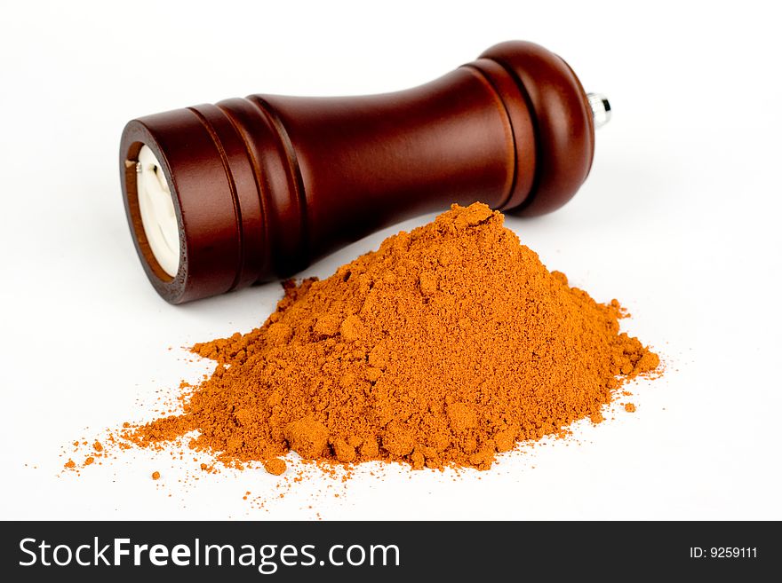 A composition of a wooden hand mill for grinding and a little of ground red pepper on a white background. A composition of a wooden hand mill for grinding and a little of ground red pepper on a white background