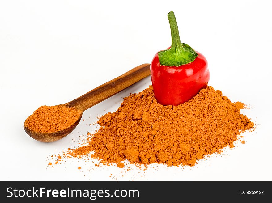 A cut pod of red hot pepper in ground pepper and a wooden spoonful of ground pepper on a white background. A cut pod of red hot pepper in ground pepper and a wooden spoonful of ground pepper on a white background
