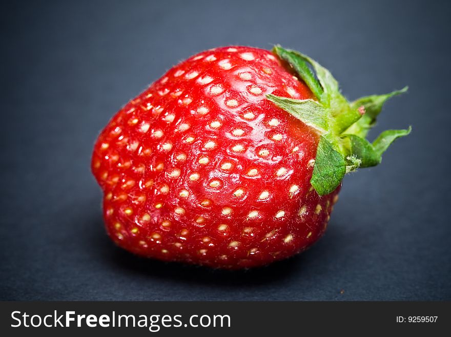 A signle strawberry fruit isolated on a plain dark background