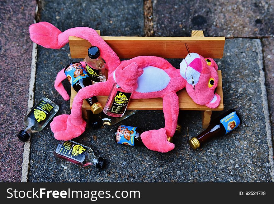 A pink panther on a wooden bench with empty bottles.