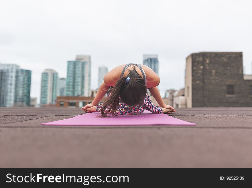 Woman performing yoga on building roof with city skyline in background.