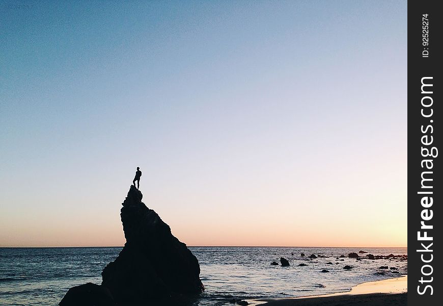 Silhouette of Person Standing on Rock on Beach Shore during Yellow Sunset