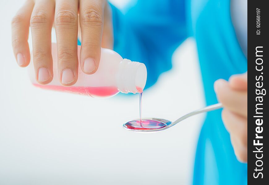 Healthcare, people and medicine concept - woman pouring medication or antipyretic syrup from bottle to spoon