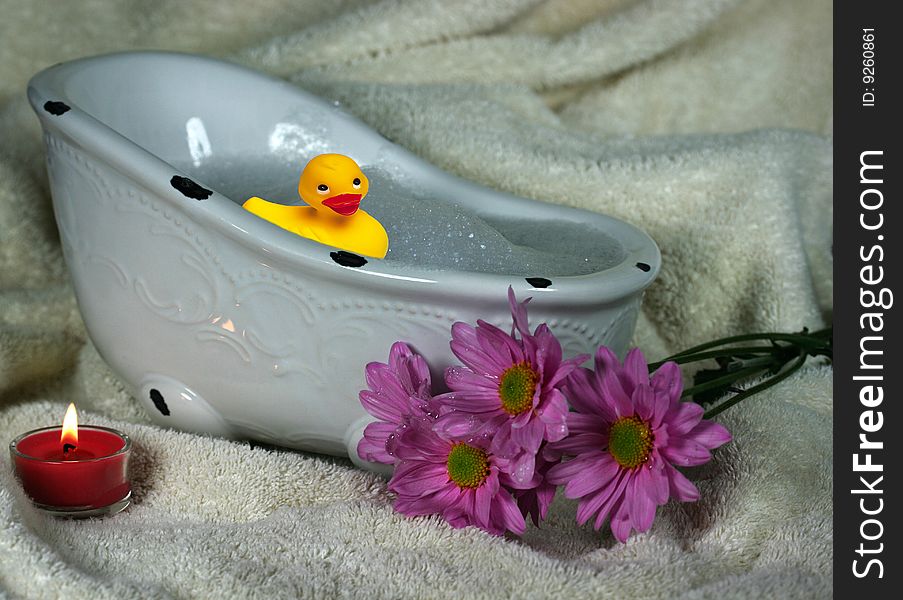 Little duckie taking a bubble bath with flowers and candle on a towel. Little duckie taking a bubble bath with flowers and candle on a towel
