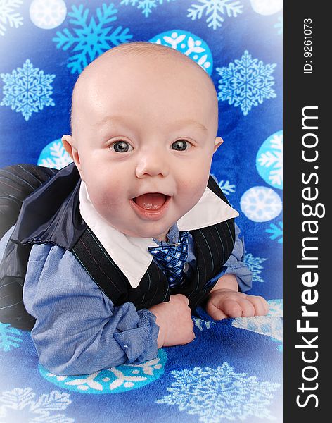 Blue eyed 5 month old smiling towards the camera. He is dressed in a suit type outfit. The photo was taken on a blue blanket with snowflakes. Blue eyed 5 month old smiling towards the camera. He is dressed in a suit type outfit. The photo was taken on a blue blanket with snowflakes.