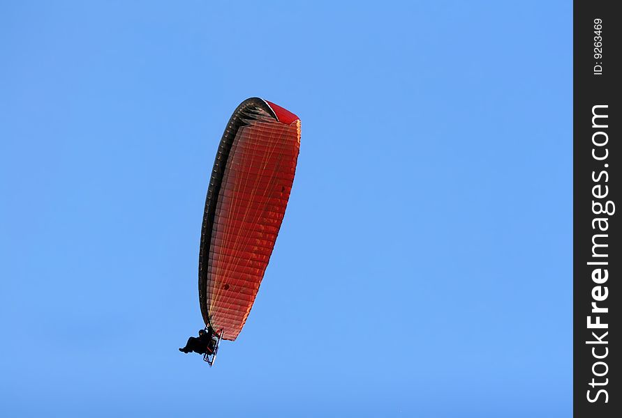 A paramotor flying high above in the blue sky. A paramotor flying high above in the blue sky