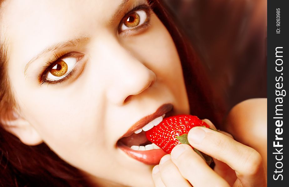 Young sexy woman, strawberry between her lips, looking at camera