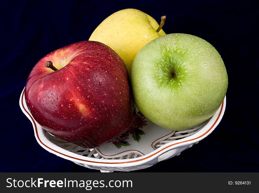 Three apples in a vase, are photographed on a dark blue background