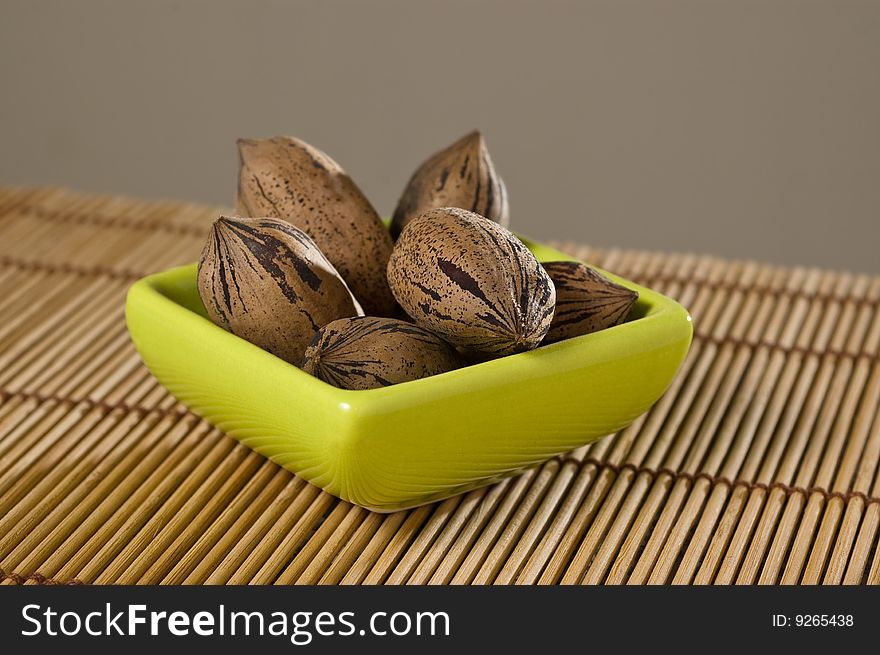 Pecan nuts (Carya illinoinensis), in a bowl, on a bamboo mat, close up. Pecan nuts (Carya illinoinensis), in a bowl, on a bamboo mat, close up.