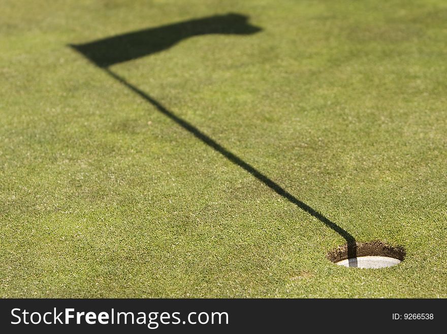 Amazing green golf field showing the hole and the flag shadow, without ball and flag (concept photography)