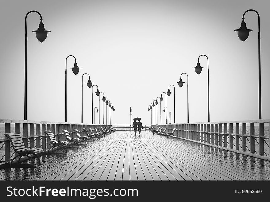 A couple walking on a pier in the rain. A couple walking on a pier in the rain.