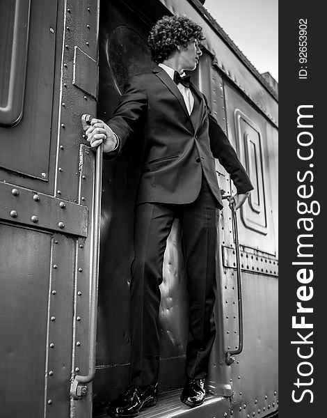 A man wearing a suit standing on the doorway of a train. A man wearing a suit standing on the doorway of a train.