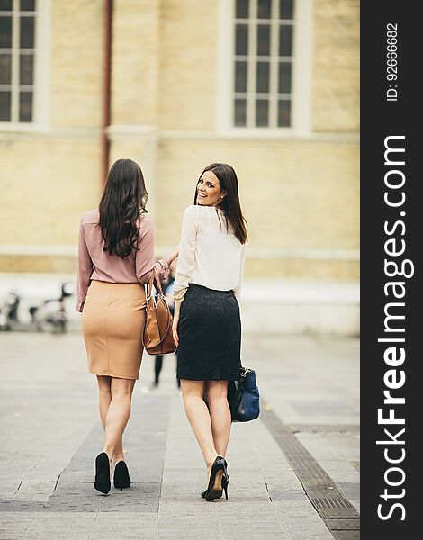 Two young women in high heels walking down the street, while one of them turned