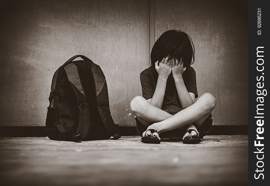 Sad Kid sitting on the floor with school bag waiting for parent.