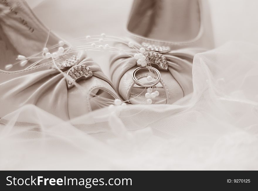 Wedding shoes decorated with beads and wedding rings in white and gray background