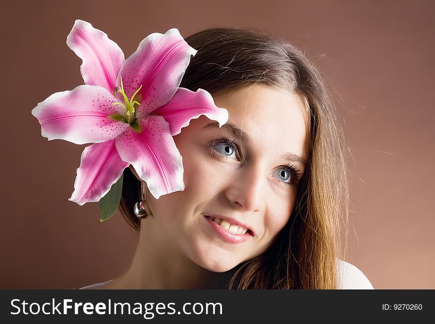 A pretty young woman with long brown hair posing with a pink lily near her face. A pretty young woman with long brown hair posing with a pink lily near her face