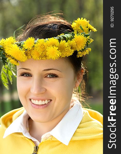 The nice young smiling girl with a garland of yellow dandelions. The nice young smiling girl with a garland of yellow dandelions