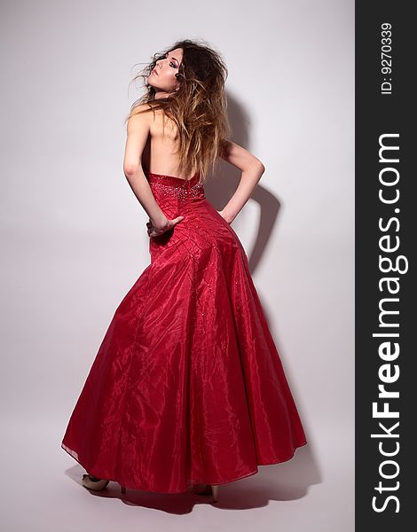 Fashion elegant young woman in red dress is dancing on grey