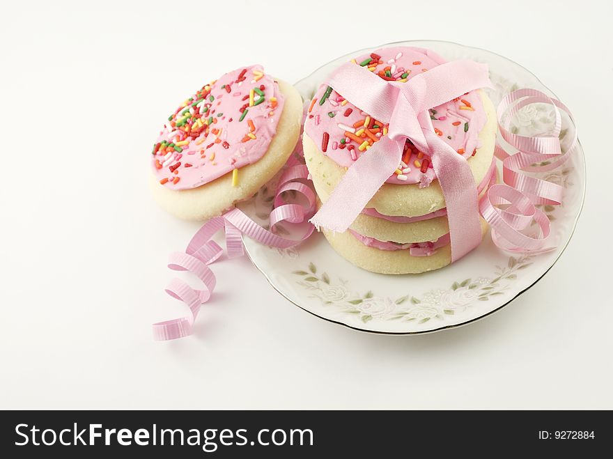 A plate of frosted pink sugar cookies with sprinkles in a stack tied with pink ribbon, isolated on white background with copy space. A plate of frosted pink sugar cookies with sprinkles in a stack tied with pink ribbon, isolated on white background with copy space
