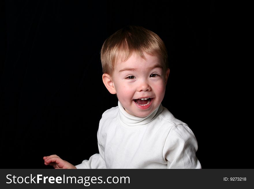 A happy toddler boy in a white shirt on a black background. A happy toddler boy in a white shirt on a black background.