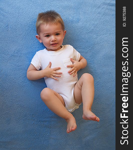 Baby boy laying on his back on a blue blanket, and wearing white. Baby boy laying on his back on a blue blanket, and wearing white.