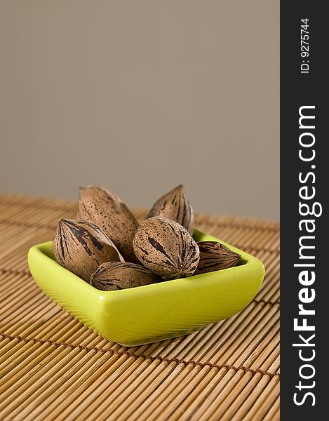 Pecan nuts (Carya illinoinensis), in a bowl, on a bamboo mat, close up. Pecan nuts (Carya illinoinensis), in a bowl, on a bamboo mat, close up.