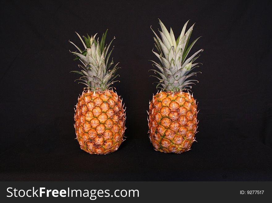 Two pineapples sit next to each other on a black backdrop.