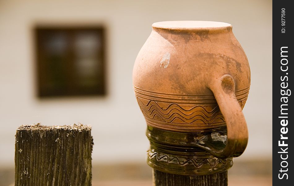 Old earthen pitcher on  wodden paling. Typical rural scene on Slovakia 100 years ago. Old window on background. Old earthen pitcher on  wodden paling. Typical rural scene on Slovakia 100 years ago. Old window on background.