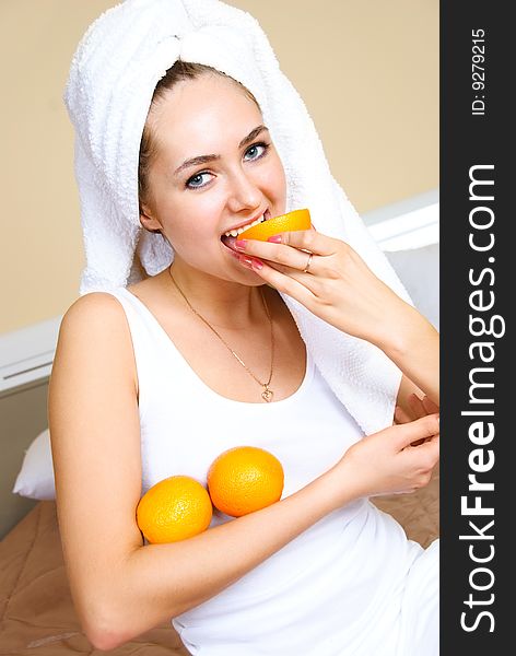 Pretty young woman sitting on the bed at home and eating oranges. Pretty young woman sitting on the bed at home and eating oranges