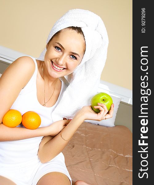 Pretty young woman sitting on the bed at home and eating oranges and an apple. Pretty young woman sitting on the bed at home and eating oranges and an apple