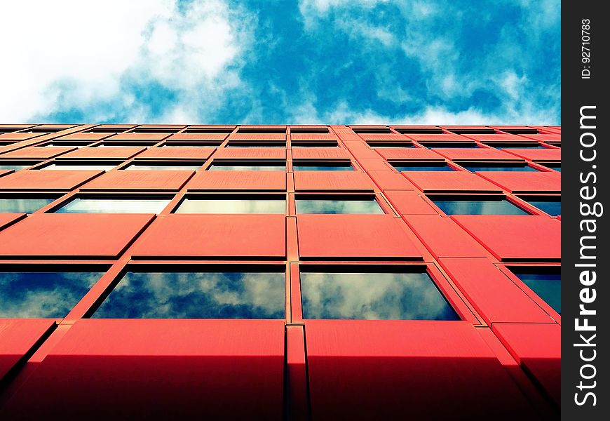 Architectural design with concrete, steel and glass and red panels (thermal cladding perhaps) livened by blue sky and white clouds reflected in the glass windows. Architectural design with concrete, steel and glass and red panels (thermal cladding perhaps) livened by blue sky and white clouds reflected in the glass windows.