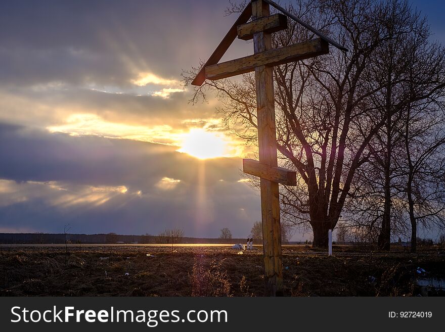A wooden cross at sunset in a field