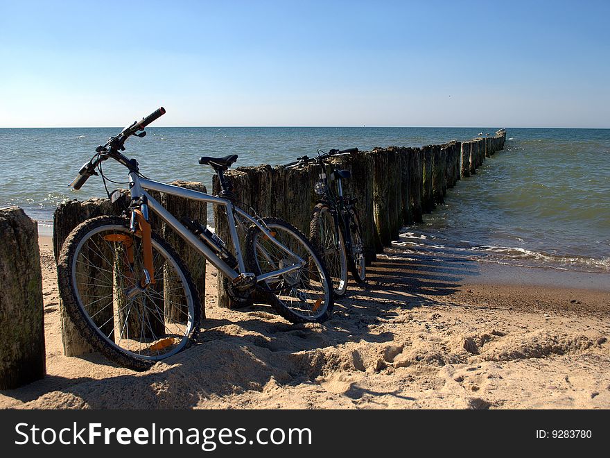 Two bicycles on a beach near a wooden breakwater. Two bicycles on a beach near a wooden breakwater