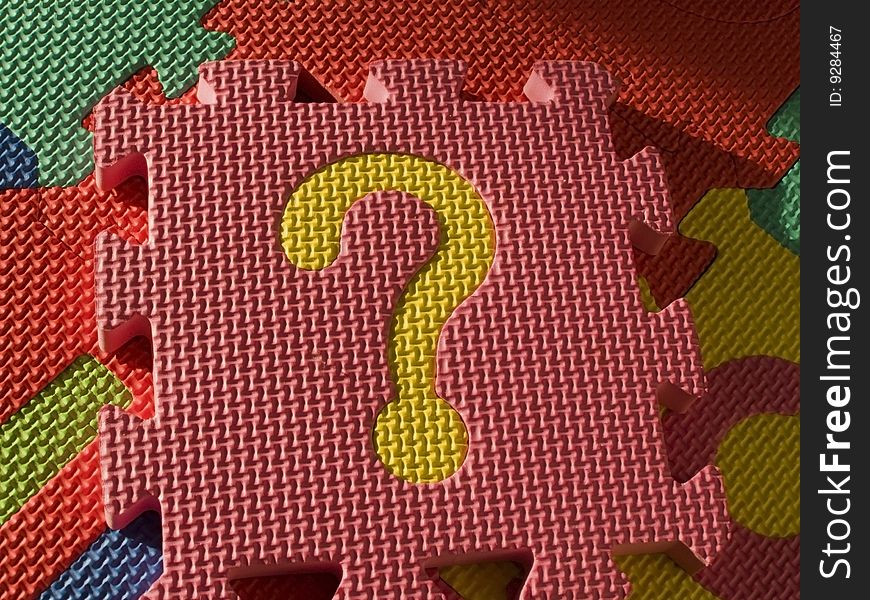 Jigsaw, pink puzzle with a bright yellow question mark, isolated on other colorful sponge pieces of the puzzle. Jigsaw, pink puzzle with a bright yellow question mark, isolated on other colorful sponge pieces of the puzzle