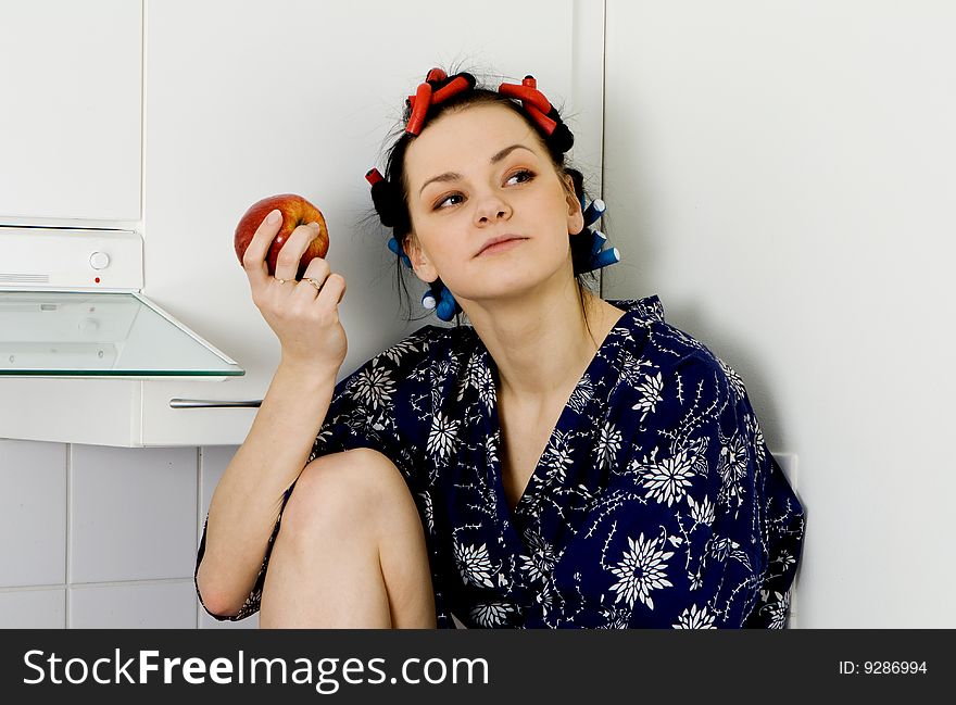 Young woman sitting in the kitchen and eating an apple. Young woman sitting in the kitchen and eating an apple
