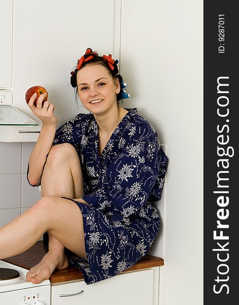 Young woman sitting in the kitchen and eating an apple. Young woman sitting in the kitchen and eating an apple