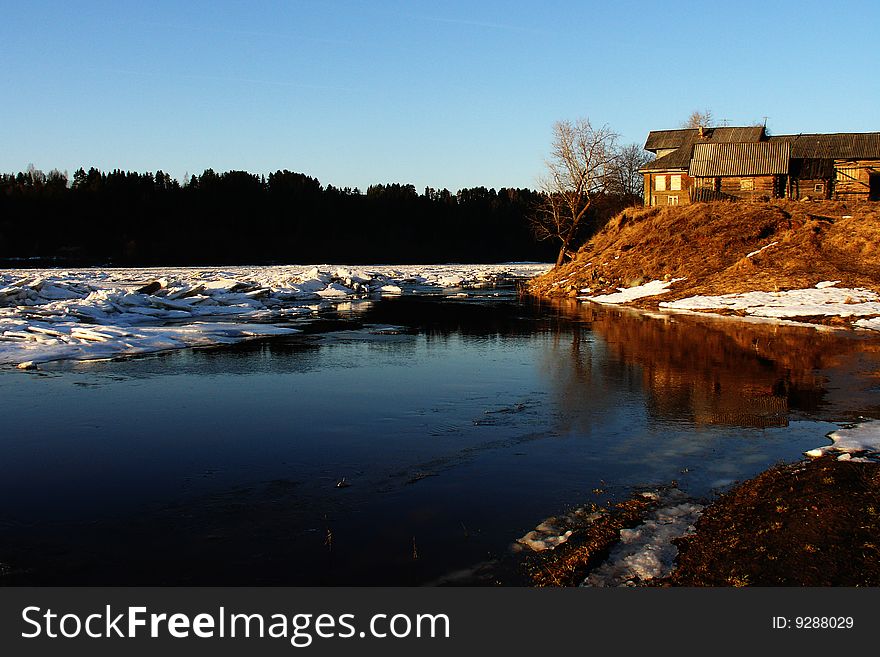 An old shed next to a snowy river bank in the mountains.