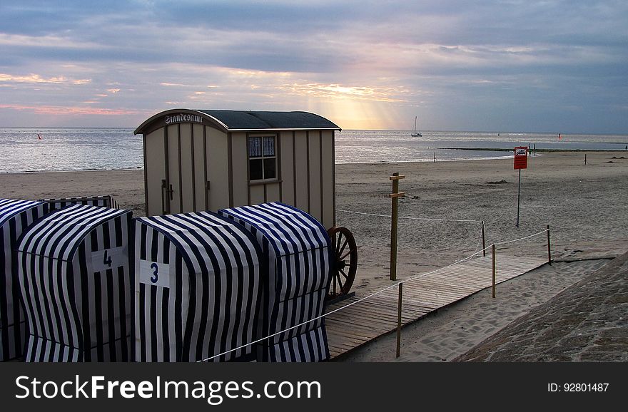 Comfort stations and a boardwalk path on the beach in the left foreground, with a beach, ocean and sky landscape in the distant background. Comfort stations and a boardwalk path on the beach in the left foreground, with a beach, ocean and sky landscape in the distant background.