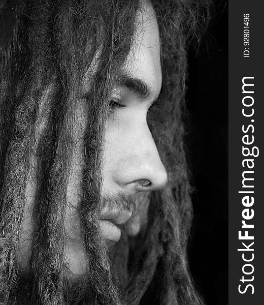 Closeup black and white profile of a serious young man with dreadlocks isolated on a dark background. Closeup black and white profile of a serious young man with dreadlocks isolated on a dark background.