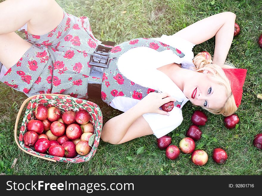 Woman in Gray and White Rose Print Onesies Laying on Grass Beside Red Apple Fruits