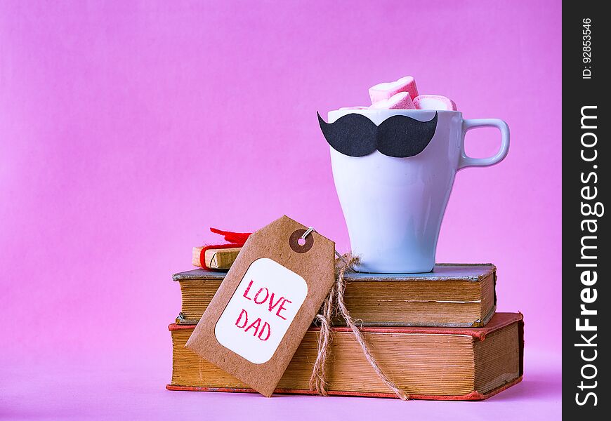 Father`s day concept. LOVE DAD alphabet on stack of books, gifts, tea cup with black Mustache on pink background