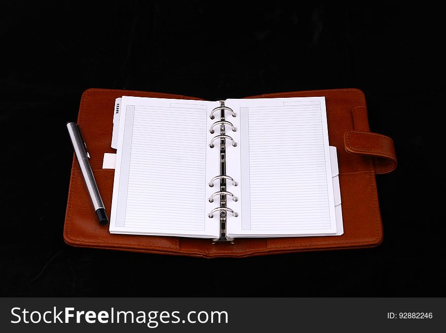 Good quality red leather notebook or diary or planner, open showing two blank pages with ring binding, and with silver pen and dark background. Good quality red leather notebook or diary or planner, open showing two blank pages with ring binding, and with silver pen and dark background.
