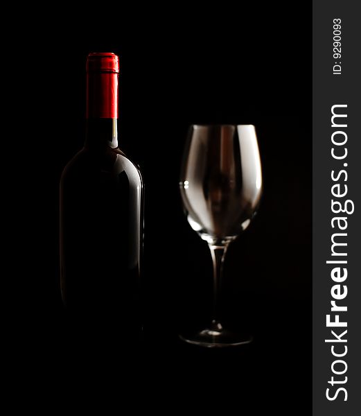 A wine bottle and an empty glass on a dark background. A wine bottle and an empty glass on a dark background.