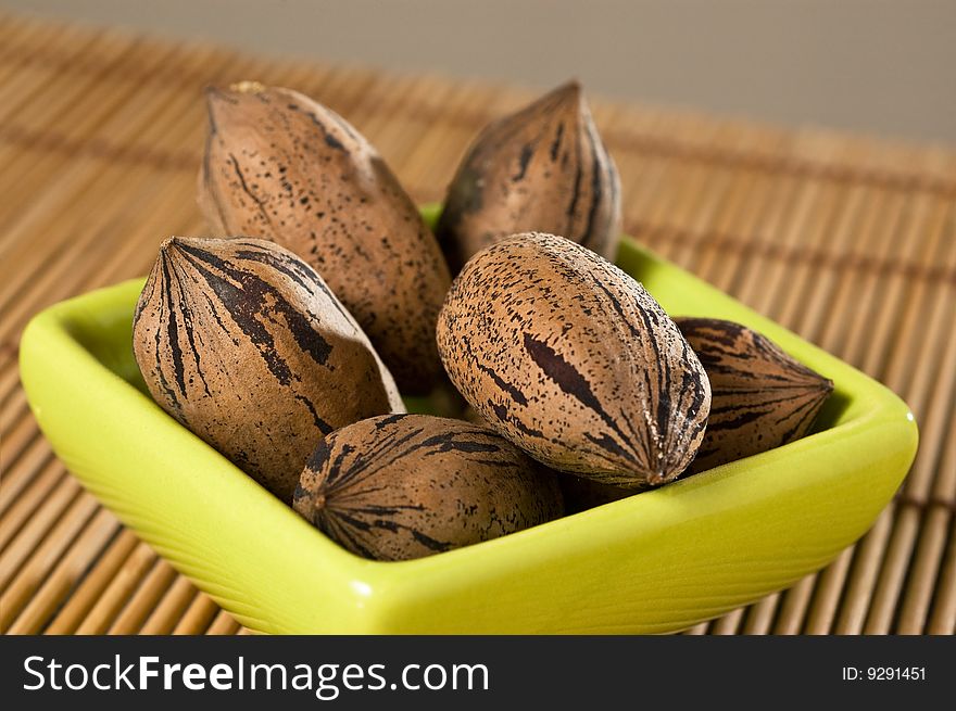 Pecan nuts (Carya illinoinensis), in a bowl, on a bamboo mat, close up.