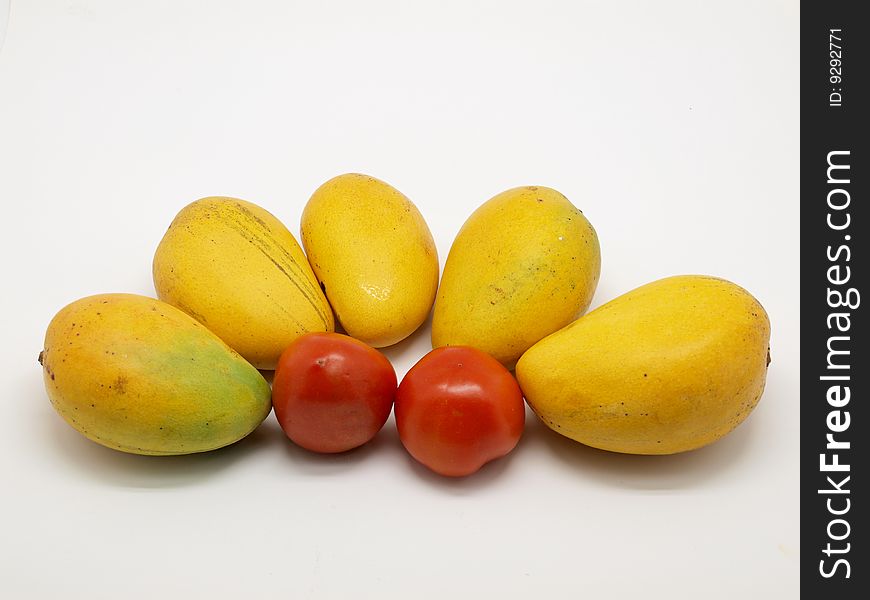 Yellow ripe mangoes and two tomatoes isolated over white background.